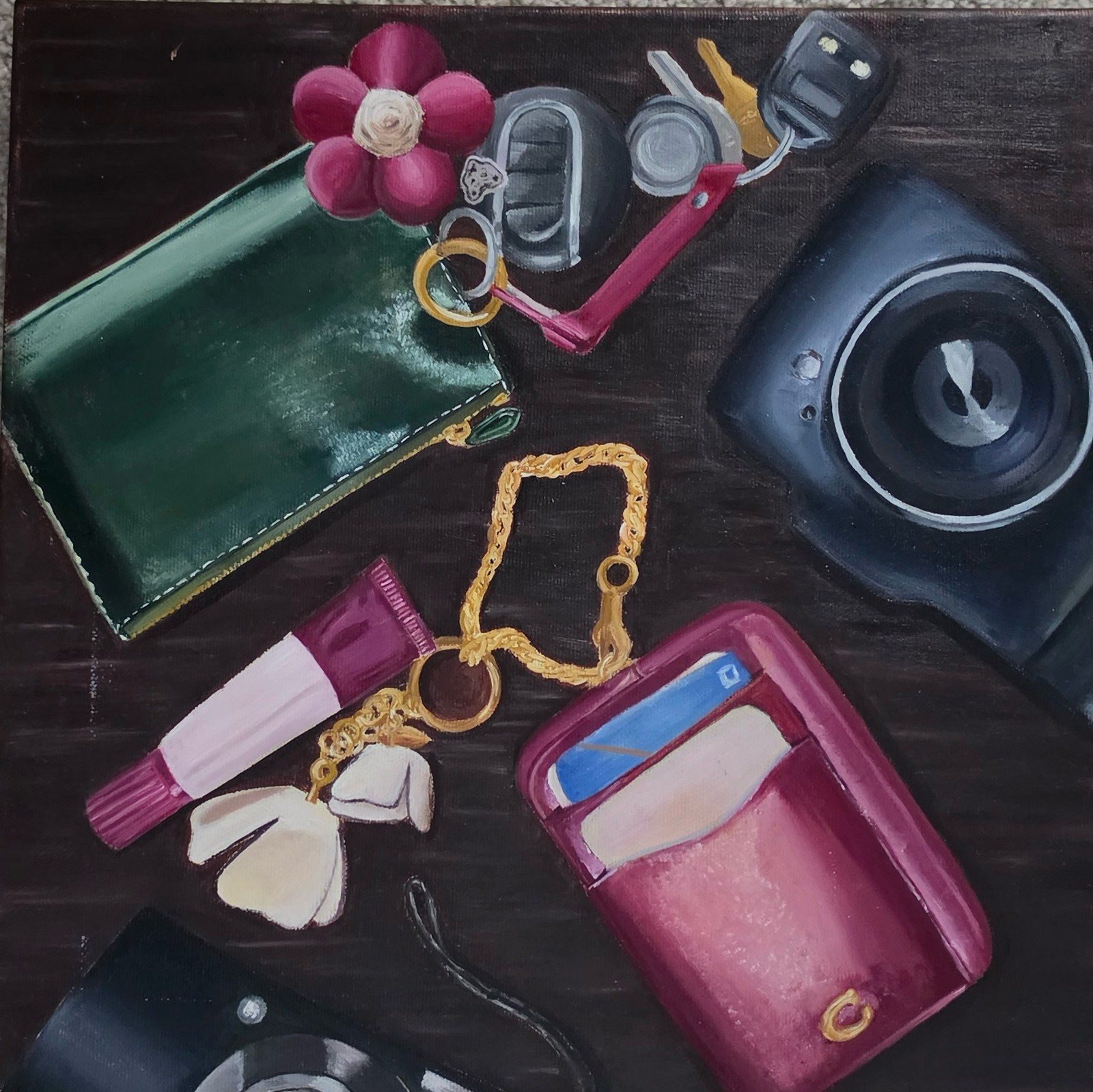 Still life on a dark table: cameras, wallets, keys, a gold chain, a flower hair clip, and a pink card holder.